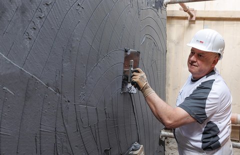 ISOTEC Mitarbeiter trägt graue Masse auf Wand auf.